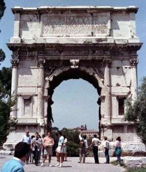 L’Arc de Titus (IV) : un arc en pierre unique qui se tient 15 mètres, avec divers touristes entourant la base. 