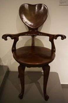 Chaise en chêne, conçue en 1906 : Chaise en bois sombre avec un dossier en forme de cœur et des accoudoirs courbés.