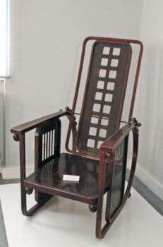 Fauteuil Sitzmaschine (1905) -Josef Hoffmann : Un fauteuil en bois sombre avec deux trous sur neuf le long du dossier.