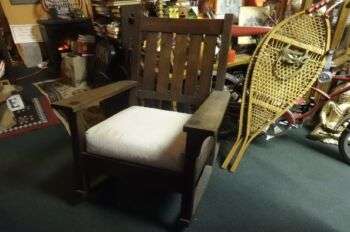 Gustave Stickley Rocker: A dark wood rocking chair with a white cushion. 