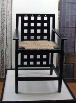 Siège de C.R. Mackintosh (The Lighthouse, Glasgow): Photo of a black chair with squares cut out of the back and a brown weaved seat