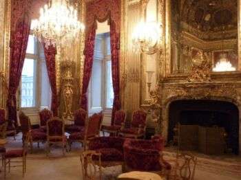 Napoleon III Apartments, which has tall, red curtains, ornate chandeliers, and a large mirror above a fireplace.