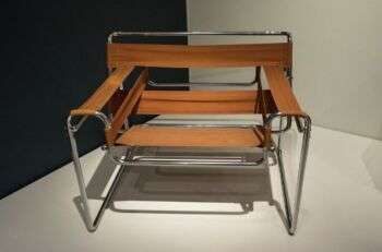 Wassily Chair (1925) by Marcel Breuer: A simple metal and tan-fabric chair with rectangles of fabric in stripes. 