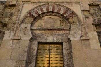 A horseshoe arch in a tan, stone mosque. Although the stone is fading in color, the door is a vibrant yellow. 