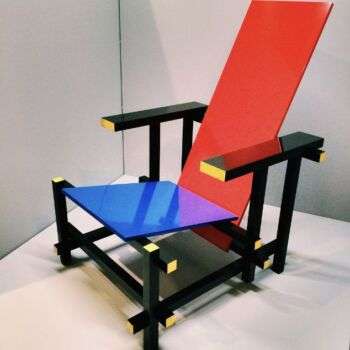 Red Blue chair (1917-1918) by Gerrit Rietveld: A photo of the red-backed chair with a blue and purple seat, and black arms and legs with yellow accents along the edges. 